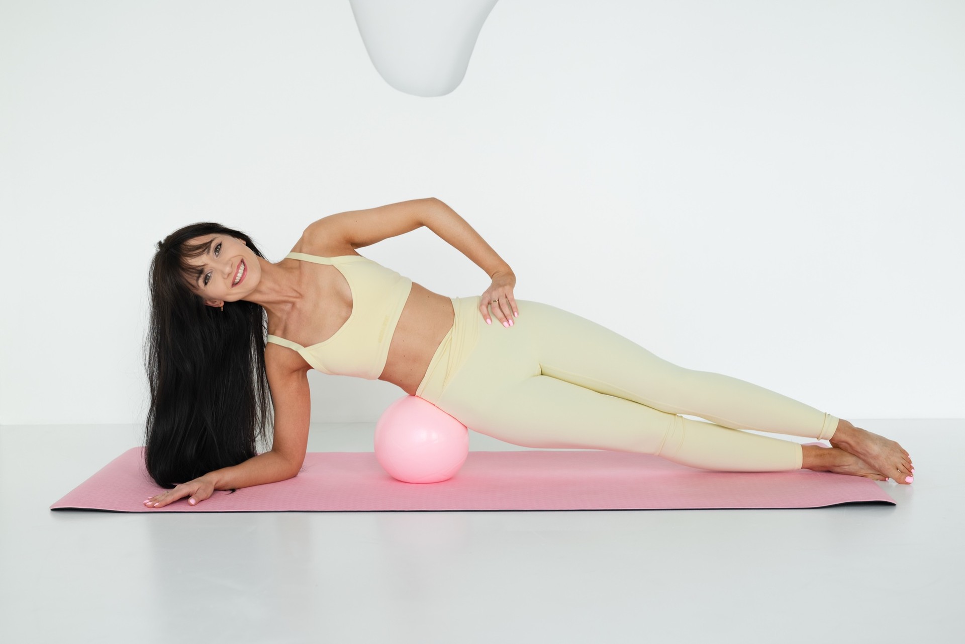 Karolina w podporze bokiem na różowej macie, z małą piłką do pilatesu pod biodrem
